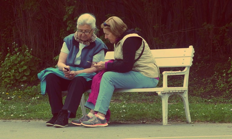 Two women on a bench looking at phones. CC0 Public Domain